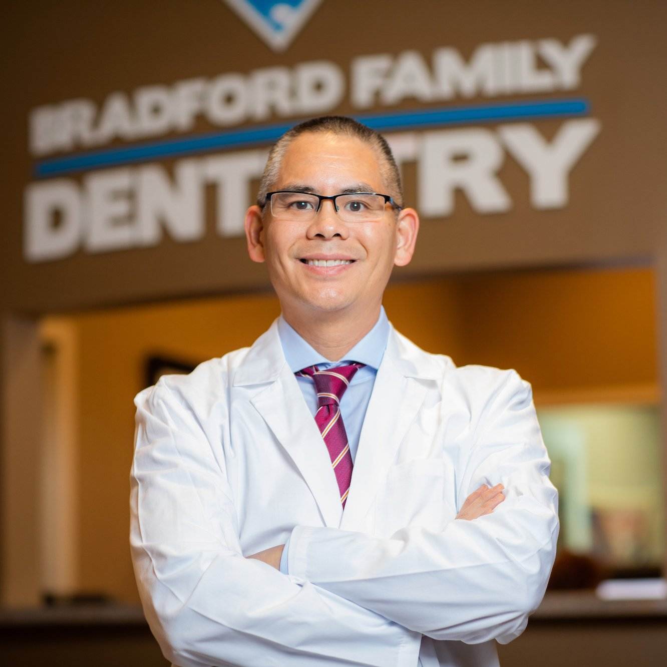 Dentist in white coat smiling confidently with arms crossed, showcasing Bradford Family Dentistry background, emphasizing professional dental practice marketing.