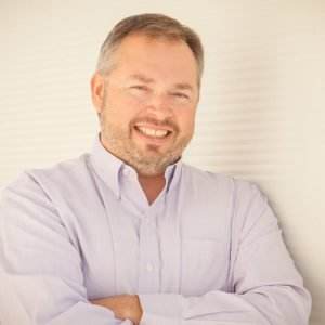 Smiling man in a light purple shirt, promoting Dental Marketing Heroes' resources for dental practice marketing success.
