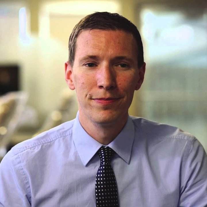 Dr. Jake DaBell, smiling in a professional setting, wearing a light blue shirt and polka dot tie, promoting effective dental marketing strategies.
