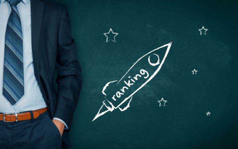 A man in a suit standing next to a chalkboard with the words ranking and SEO Services written on it.