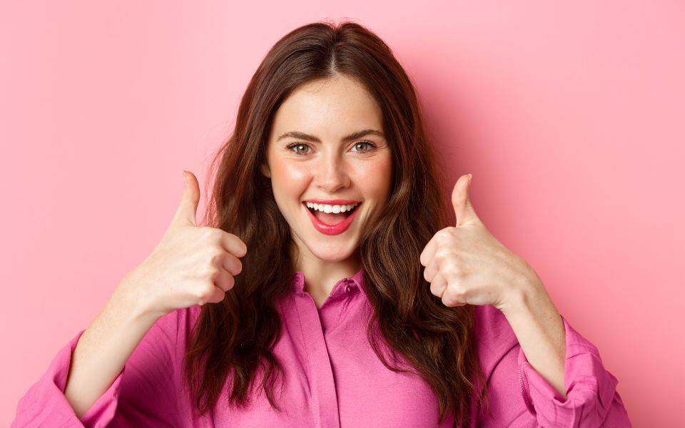 Young woman giving thumbs up on pink background.