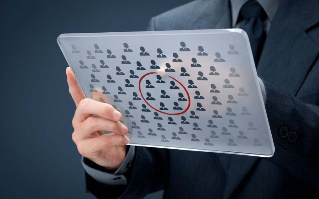 A person in a suit holds a transparent tablet displaying multiple icons of people, with one icon circled in red.
